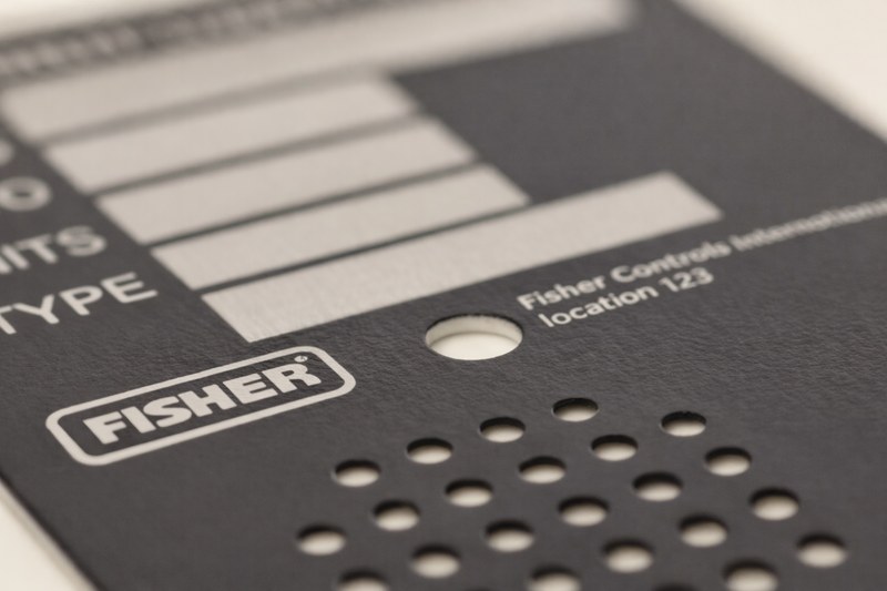 Black aluminum control panel nameplate manufactured by Metallics, Inc. for Fisher, featuring etched identification text, specification fields, and precision-cut openings.