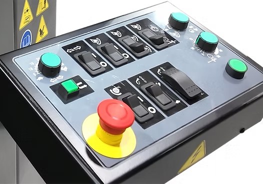 Industrial machine control panel featuring graphic overlays and labeled controls manufactured by Metallics, Inc., including switches, indicator icons, and an emergency stop button.